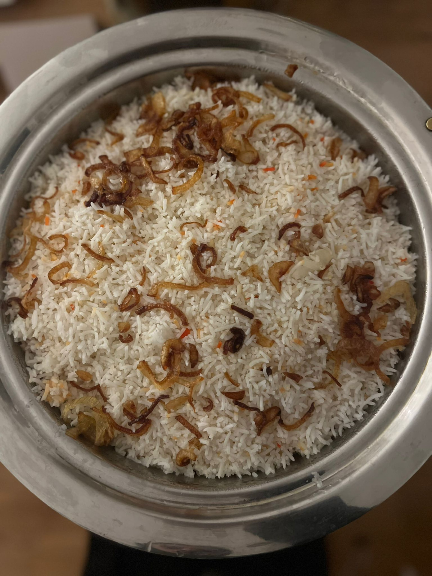 A large service pot of basmati pilau rice topped with crisp fried onions, ready for the buffet